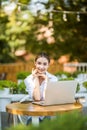 Beautiful young woman with cup of coffee sitting at outdoor cafe and reading new mails on laptop, Blogger woman using laptop at ou Royalty Free Stock Photo