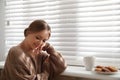 Beautiful young woman with cup of hot drink and cookies near window. Winter atmosphere Royalty Free Stock Photo