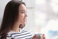 Beautiful young woman with cup of hot tea near window at home Royalty Free Stock Photo