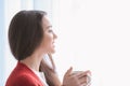 Beautiful young woman with cup of hot tea near window at home Royalty Free Stock Photo