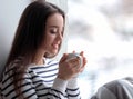 Beautiful young woman with cup of hot tea near window at home Royalty Free Stock Photo