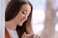 Beautiful young woman with cup of hot tea near window at home Royalty Free Stock Photo