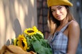 Beautiful young woman with dark hair in a hat, in the city, holding hands for a bouquet of sunflowers and looking away. Royalty Free Stock Photo