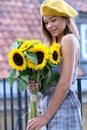 Beautiful young woman with dark hair in a hat, in the city, holding hands for a bouquet of sunflowers and looking away. Royalty Free Stock Photo