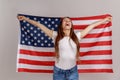 Beautiful young woman with dark hair, holding USA flag over shoulders, rejoicing happily. Royalty Free Stock Photo