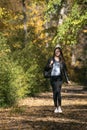 Beautiful young woman with dark hair walks along the alley of autumn park and enjoys a warm day. Lonely girl in forest Royalty Free Stock Photo