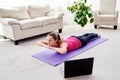 Beautiful young woman doing exercise for back on floor at home, online training on laptop computer, copy space. Royalty Free Stock Photo