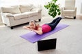 Beautiful young woman doing exercise for back on floor at home, online training on laptop computer, copy space. Royalty Free Stock Photo