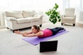 Beautiful young woman doing exercise for back on floor at home, online training on laptop computer, copy space. Royalty Free Stock Photo