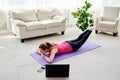 Beautiful young woman doing exercise for back on floor at home, online training on laptop computer, copy space. Royalty Free Stock Photo