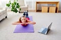 Beautiful young woman doing exercise for back on floor at home, online training on laptop computer, copy space. Royalty Free Stock Photo