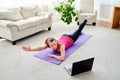 Beautiful young woman doing exercise for back on floor at home, online training on laptop computer, copy space. Royalty Free Stock Photo