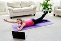 Beautiful young woman doing exercise for back on floor at home, online training on laptop computer, copy space. Royalty Free Stock Photo