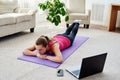 Beautiful young woman doing exercise for back on floor at home, online training on laptop computer, copy space. Royalty Free Stock Photo