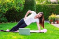 Beautiful young woman doing sport in garden outdoors following guide of online tutorial or trainer on laptop. Royalty Free Stock Photo