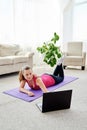 Beautiful young woman doing working out exercise on floor at home and using laptop, online training, copy space. Royalty Free Stock Photo