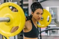 Beautiful young woman doing workout in the gym, pushing yellow barbell on shoulders. Female hard workout for cross fit. People,