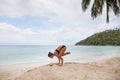 Beautiful young woman is doing yoga near the sea and drinks coconut