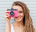 Beautiful young woman with dreadlocks taking photos with vintage pink retro film camera Royalty Free Stock Photo
