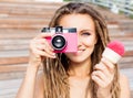 Beautiful young woman with dreadlocks taking photos with vintage pink retro film camera and pink ice-cream have fun in warm summer Royalty Free Stock Photo