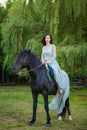 Beautiful young woman in beautiful dress on black horse in nature Royalty Free Stock Photo