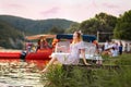 A beautiful young woman in a dress poses sitting on a river pier. A mountain and boats in the background. Summer Royalty Free Stock Photo