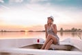 Beautiful young woman in a dress sitting on the boat and talking with her boyfriend on mobile phone in a sunset Royalty Free Stock Photo