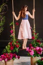 a beautiful young woman in a dress stands on a swing in peony flowers. Royalty Free Stock Photo