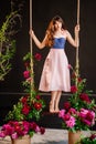 a beautiful young woman in a dress stands on a swing in peony flowers. Royalty Free Stock Photo