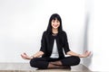 Beautiful young woman dressed in a black business suit sitting in lotus position on a floor in office, smiling, closed her eyes Royalty Free Stock Photo