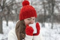 Beautiful young woman drink hot beverage from cup in winter outdoor. Girl in red hat and mittens in snowy park Royalty Free Stock Photo