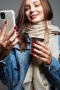 Beautiful young woman drinking coffee and looking at the phone screen. portrait of smiling girl in scarf