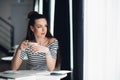 Beautiful young woman drinking coffee and looking through window while sitting at a table in a cafe. Royalty Free Stock Photo