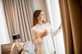 Beautiful young woman drinking coffee and looking through window while standing in the apartment Royalty Free Stock Photo