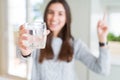 Beautiful young woman drinking a fresh glass of water very happy pointing with hand and finger to the side Royalty Free Stock Photo