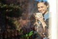 Beautiful young woman drinking morning tea or coffee while sitting near window, garden reflecting in the glass Royalty Free Stock Photo