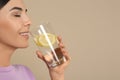 Beautiful young woman drinking tasty lemon water on beige, closeup. Space for text Royalty Free Stock Photo