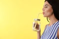 Beautiful young woman drinking tasty lemon water on yellow background, closeup. Space for text Royalty Free Stock Photo