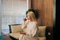 Beautiful young woman drinking tea sitting on sofa in modern cafe by window. Pretty smiling lady enjoying cup of coffee Royalty Free Stock Photo