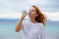 Beautiful young woman drinking water in summer beach outdoor with sea background Royalty Free Stock Photo