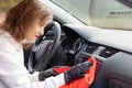 Beautiful young woman driver in a white jacket and black gloves wipes the dust in the car interior with a red rag on a bright warm Royalty Free Stock Photo