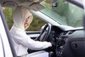 A beautiful young woman driver in a white jacket with a hood and black gloves sits at the wheel of a car. Selective focus Royalty Free Stock Photo