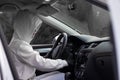 A beautiful young woman driver in a white jacket with a hood and black gloves sits at the wheel of a car. Selective focus. Portrai Royalty Free Stock Photo