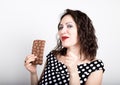 Beautiful young woman eating a chocolate bar, wears a dress with polka dots. expresses different emotions Royalty Free Stock Photo