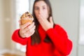 Beautiful young woman eating chocolate chips muffin cover mouth with hand shocked with shame for mistake, expression of fear, Royalty Free Stock Photo