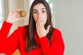 Beautiful young woman eating fresh green kiwi cover mouth with hand shocked with shame for mistake, expression of fear, scared in