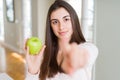 Beautiful young woman eating healthy green apple fruit pointing with finger to the camera and to you, hand sign, positive and Royalty Free Stock Photo