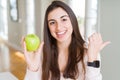 Beautiful young woman eating healthy green apple fruit pointing and showing with thumb up to the side with happy face smiling Royalty Free Stock Photo