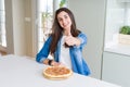 Beautiful young woman eating homemade tasty pizza at the kitchen doing happy thumbs up gesture with hand Royalty Free Stock Photo