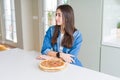 Beautiful young woman eating homemade tasty pizza at the kitchen looking to side, relax profile pose with natural face with